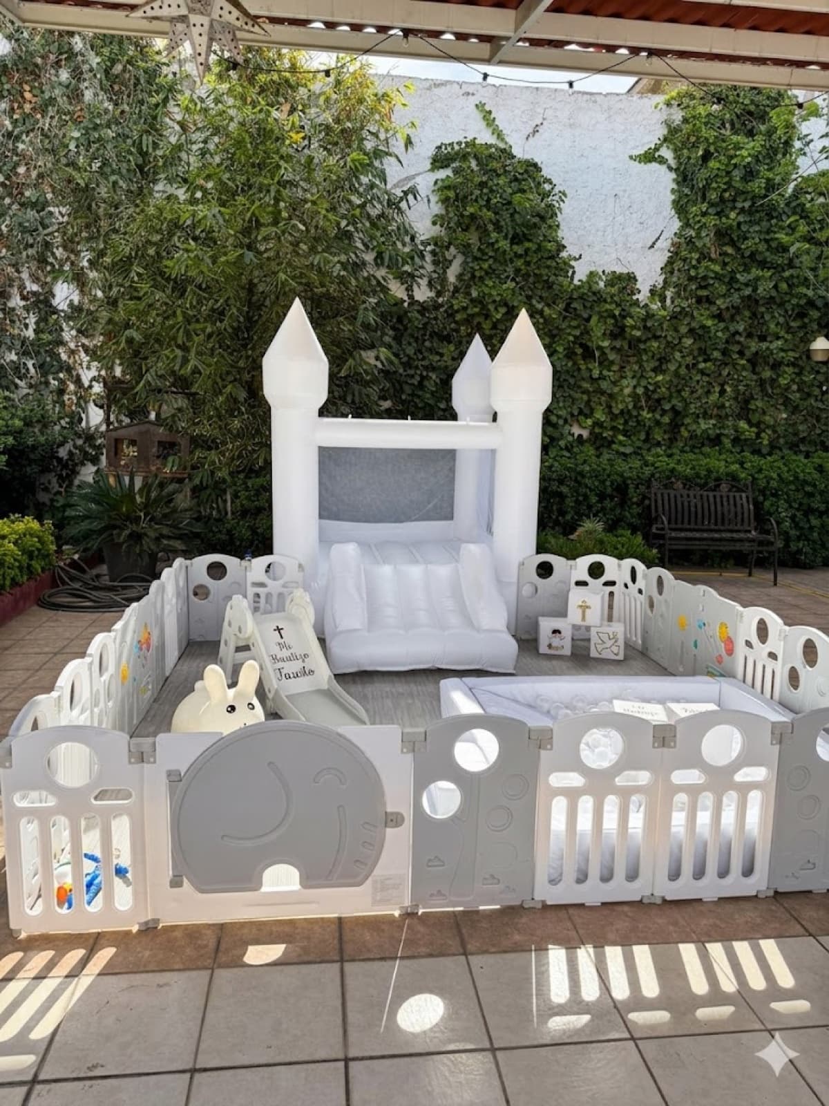 Soft play KUMA bajo pergola con castillo inflable blanco, alberca de pelotas, conejito, y resbaladilla con calcomanía personalizada 'Mi Bautizo Fausto'